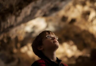 Bambino con zaino e occhiali osserva affascinato le formazioni rocciose all’interno delle Grotte di Frasassi durante una visita scolastica.