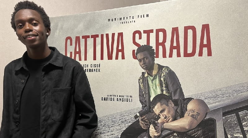 Malich Cissé davanti al poster del film Cattiva strada di Davide Angiuli con Giulio Beranek, film italiano ambientato a Bari