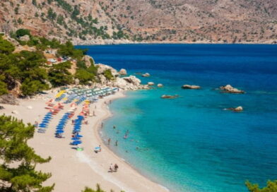 Spiaggia di Karpathos con mare cristallino e ombrelloni, vacanza a Karpathos agosto tra relax e natura incontaminata