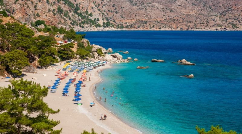 Spiaggia di Karpathos con mare cristallino e ombrelloni, vacanza a Karpathos agosto tra relax e natura incontaminata