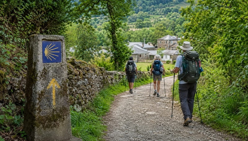 Pellegrini sul Cammino di Santiago da Sarria percorrono un sentiero nella campagna verde della Galizia, seguendo la conchiglia e la freccia gialla.