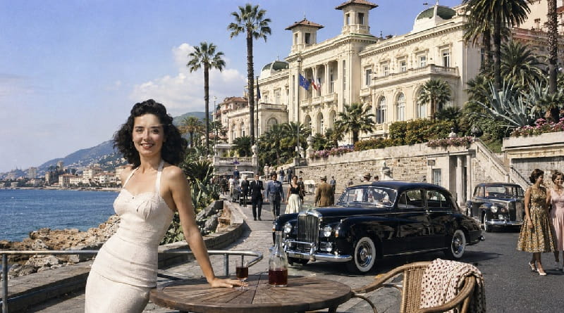 Sanremo negli anni Cinquanta con il Casinò, auto d’epoca, eleganti passanti e il Mediterraneo, simbolo della città porta della Costa Azzurra.